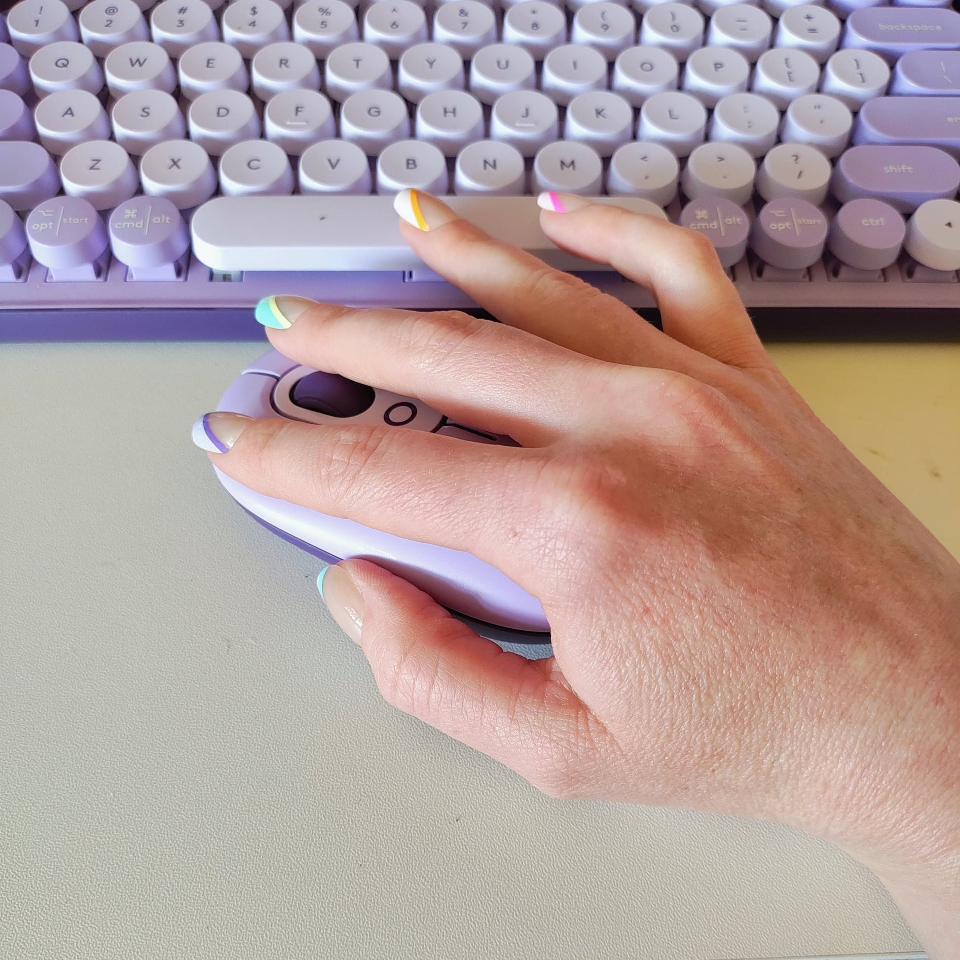 Square cut nails on right hand with angled stripes on left hand side of each nail behind using a purple mouse and keyboard. The stripes are blue, purple, green, orange and pink. 