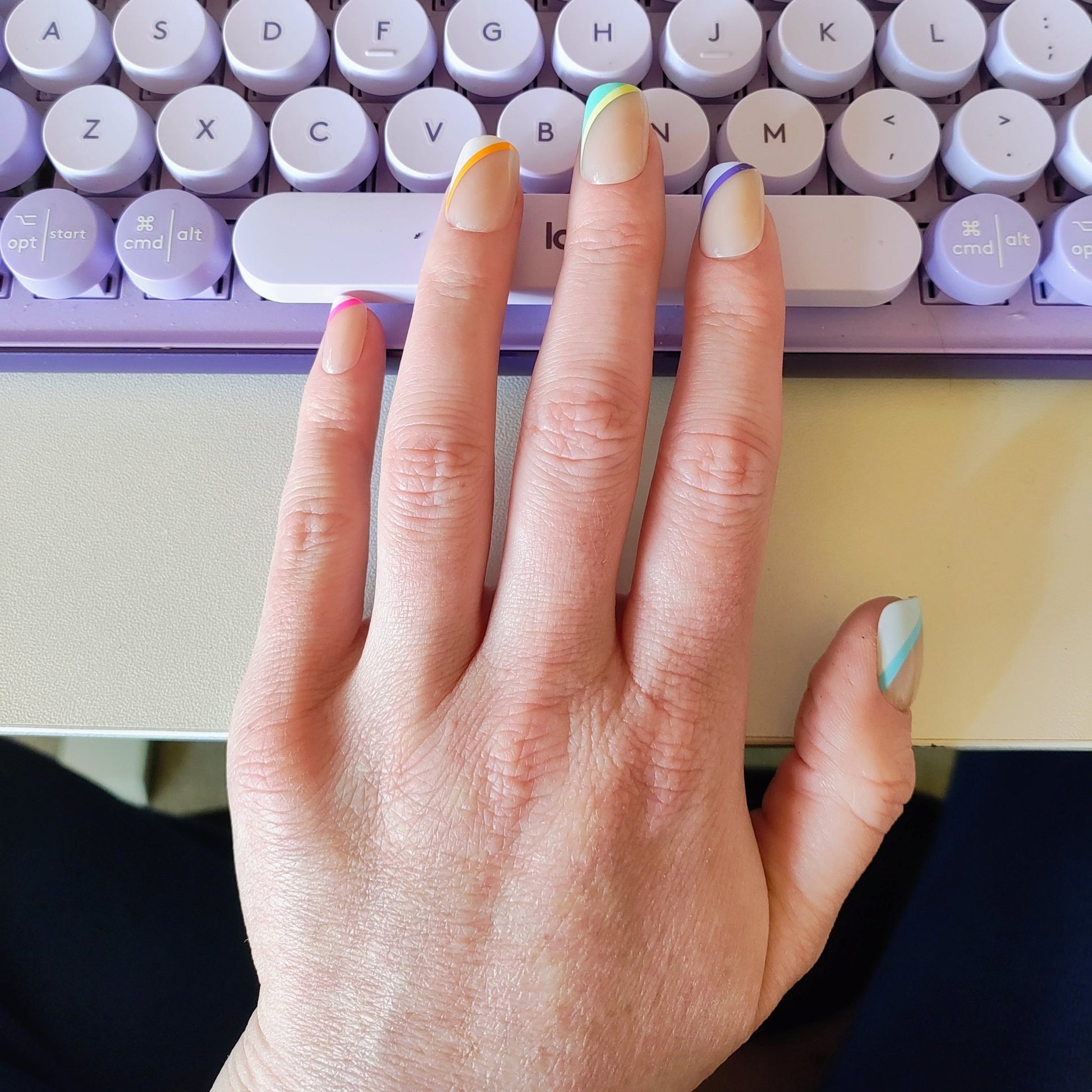 Square cut nails on left hand with angled stripes on left hand side of each nail behind using a purple keyboard. The stripes are pink, orange, green, purple and blue.