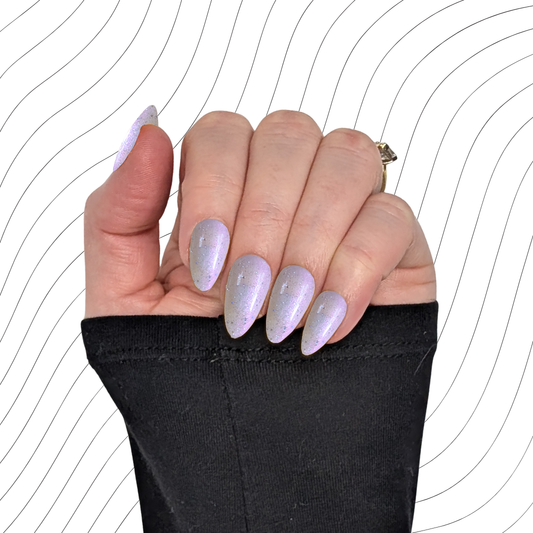 Left hand showing pearlescent white short almond nails with a glitter gloss finish on a wavy background.