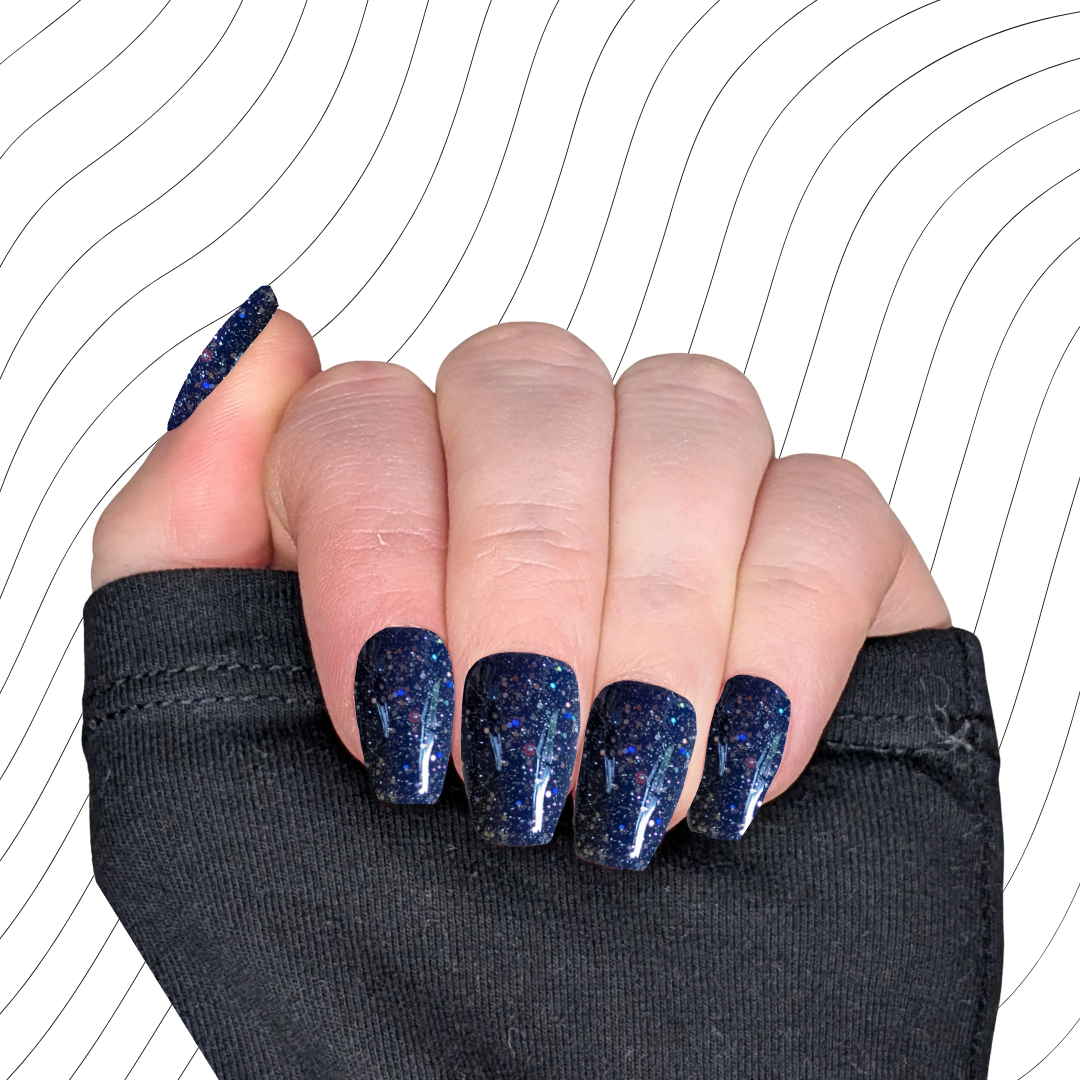 Left hand showing navy blue short coffin nails with a glitter gloss finish on a wavy background.