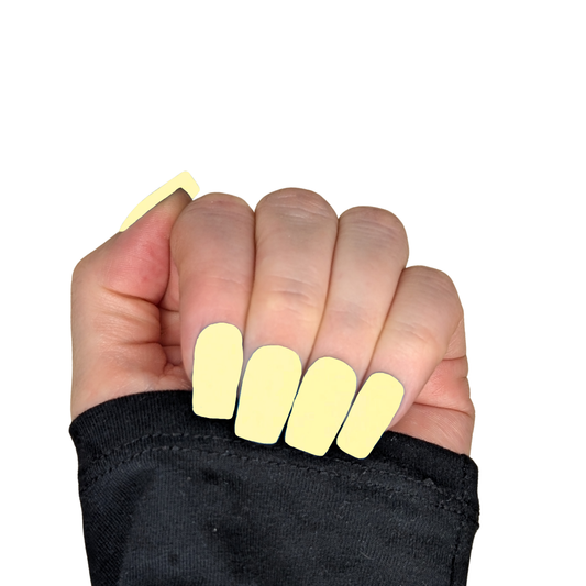 Left hand showing a pale yellow nails in a medium square length