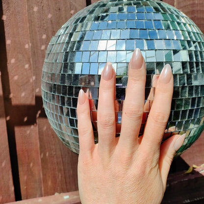 Left hand showing an almond shimmery, pinky peach coloured nails on a disco ball.