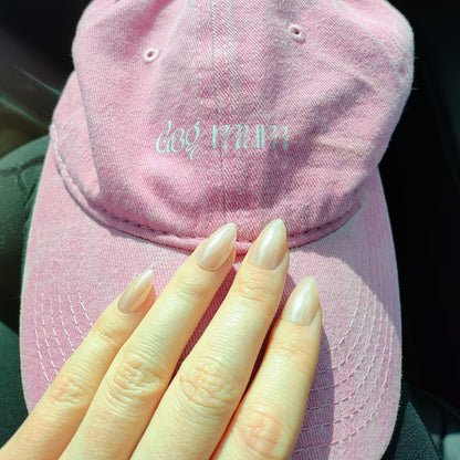 Left hand showing an almond shimmery, pinky peach coloured nails on a pink 'dog mum' hat.