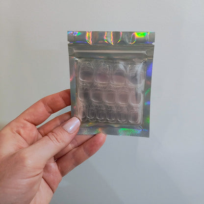 Hand holding a small silver resealable bag that has a clear front displaying sticker sheets inside.