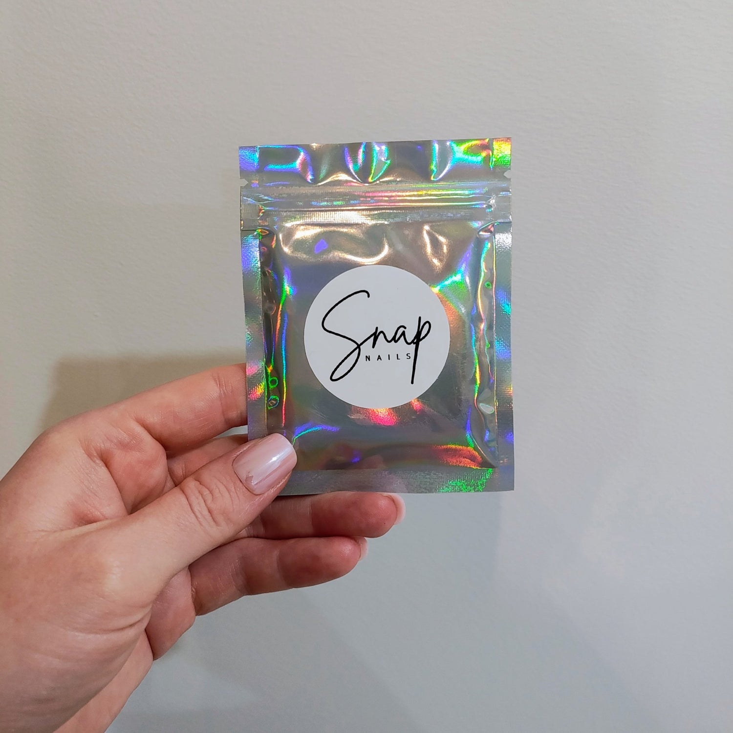 Hand holding a small silver resealable bag that has a white circle sticker with the Snap Nails logo.