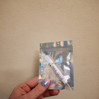 Left hand showing a silver holographic small bag with a a small glue and four nail sticker sheets.