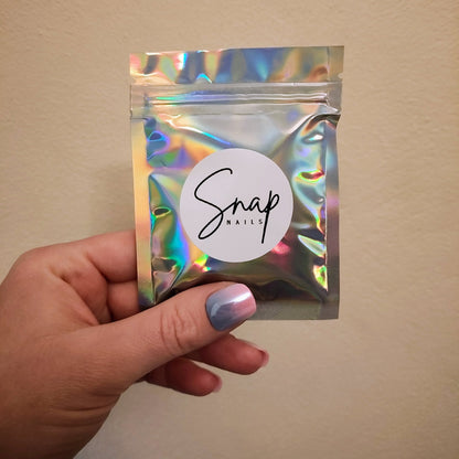Left hand showing a silver holographic small bag with a Snap Nails logo. 
