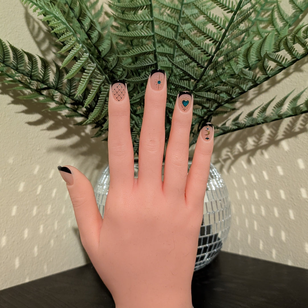 Image of a right hand wearing Snap Nails in Signature collection of 5 square black french tip nails gold details. 