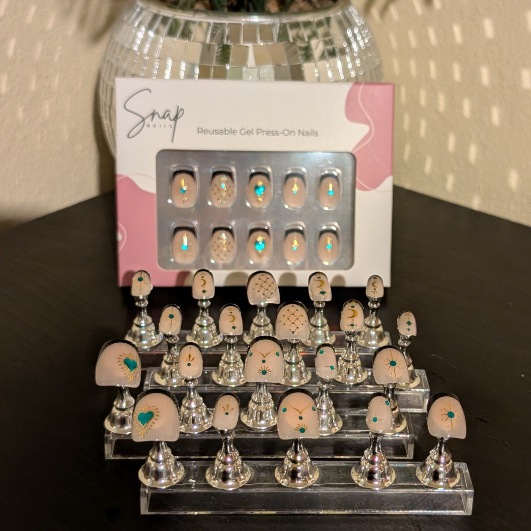 Image of 20 Snap Nails in Signature collection square black french tip nails with gold details on little nail pedestals. Above this is a box of 10 nails with a nail file and cuticle stick. 