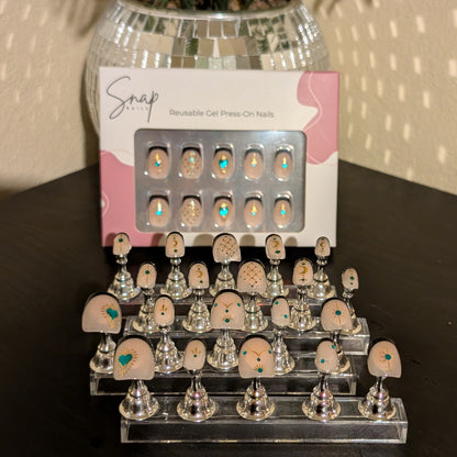 Image of 20 Snap Nails in Signature collection square black french tip nails with gold details on little nail pedestals. Above this is a box of 10 nails with a nail file and cuticle stick. 