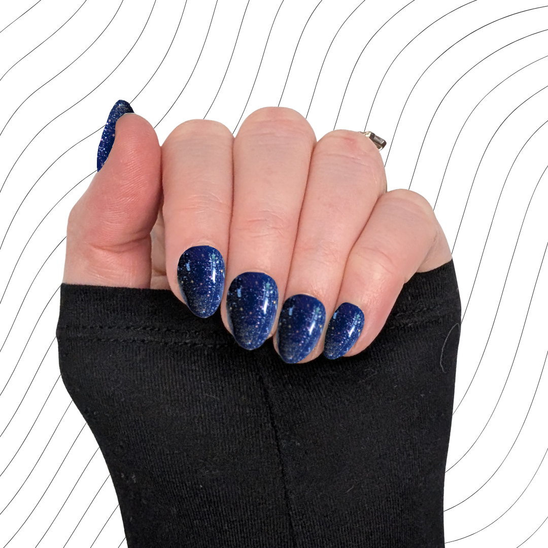 Left hand showing navy blue extra short almond nails with a glitter gloss finish on a wavy background.