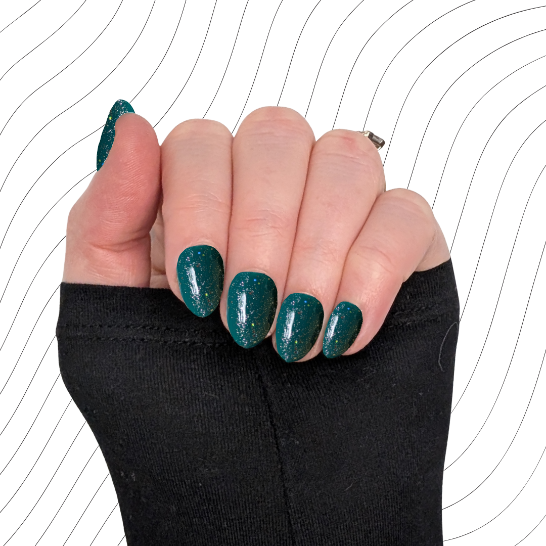 Left hand showing emerald green extra short almond nails with a glitter gloss finish on a wavy background.