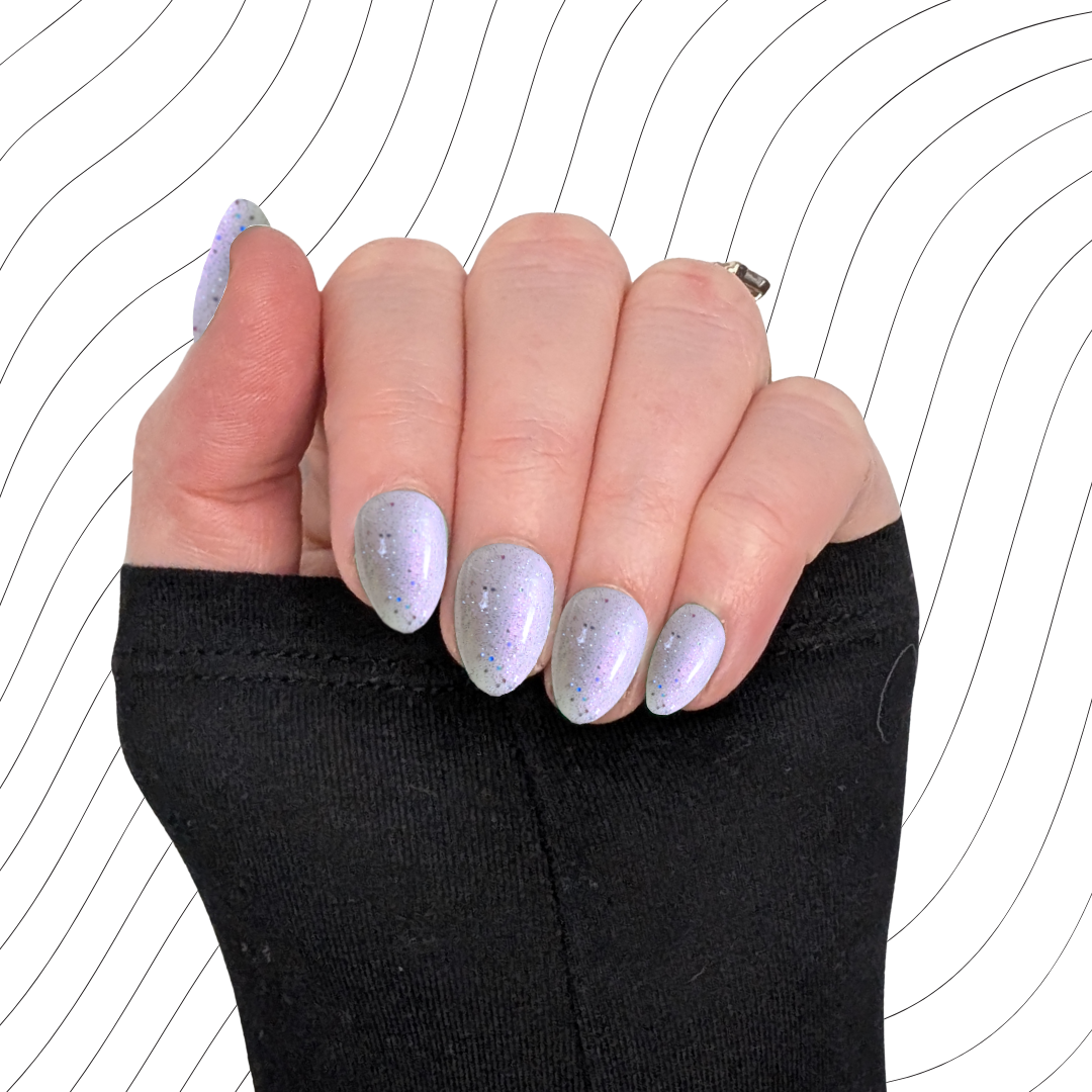 Left hand showing pearlescent white extra short almond nails with a glitter gloss finish on a wavy background.