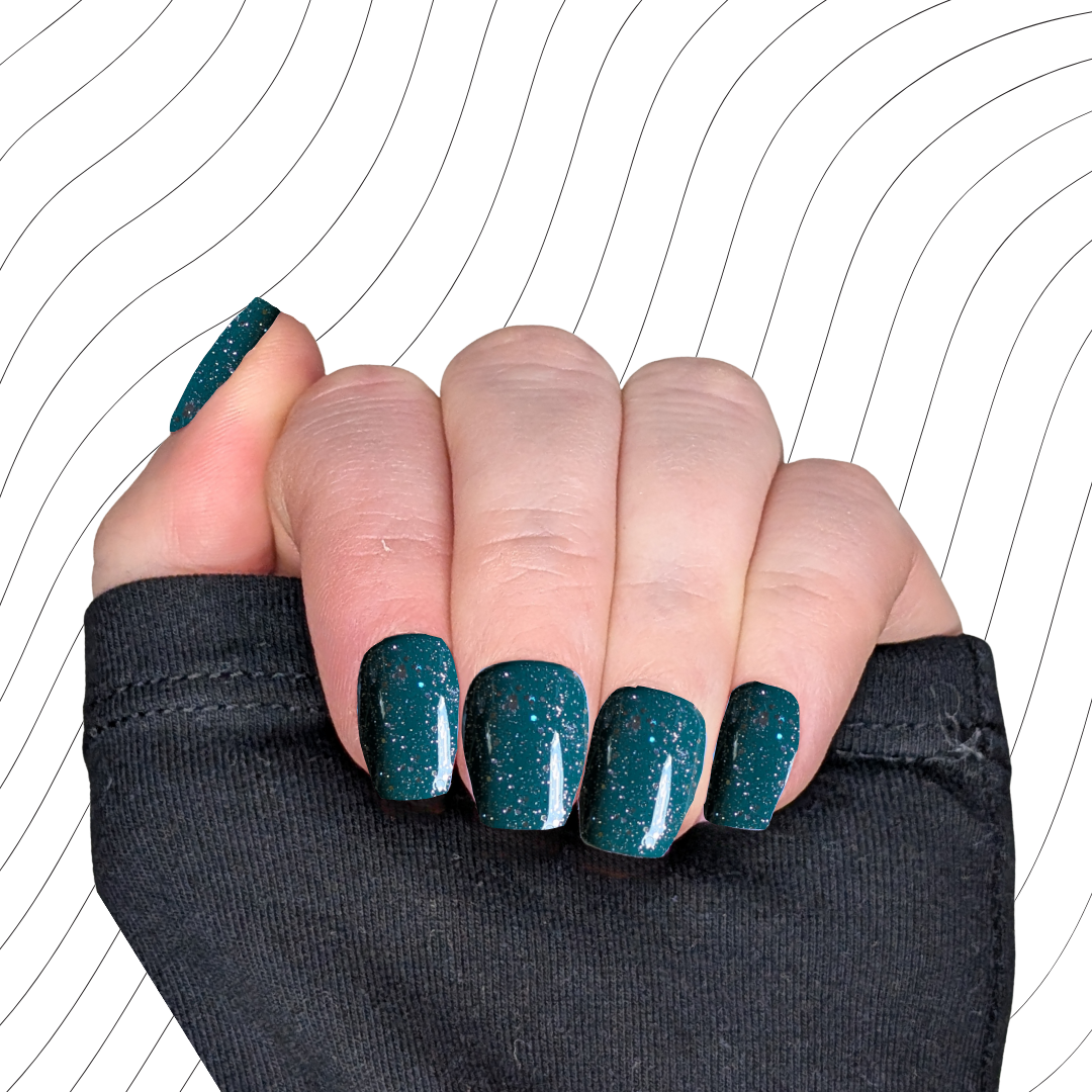 Left hand showing emerald green extra short coffin nails with a glitter gloss finish on a wavy background.