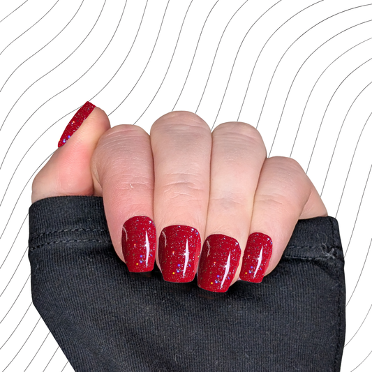Left hand showing deep red extra short coffin nails with a glitter gloss finish on a wavy background.