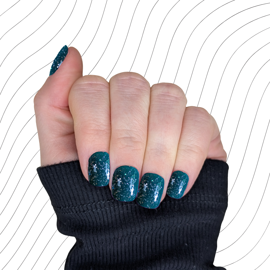 Left hand showing emerald green extra short square nails with a glitter gloss finish on a wavy background.