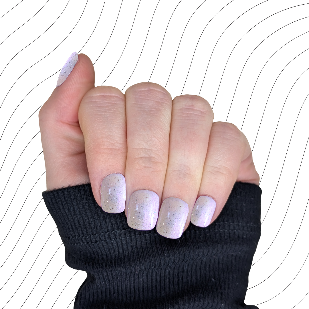 Left hand showing pearlescent white extra short square nails with a glitter gloss finish on a wavy background.