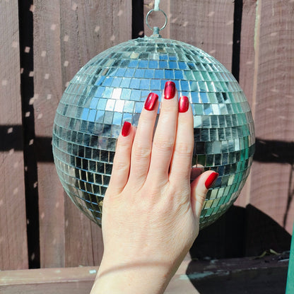 Hand behind a disco ball showing deep cherry red square nails