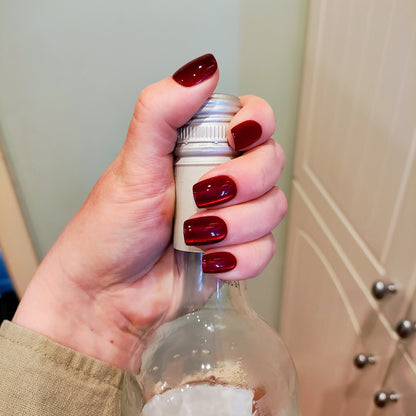 Hand holding top of wine bottle showing deep cherry red square nails