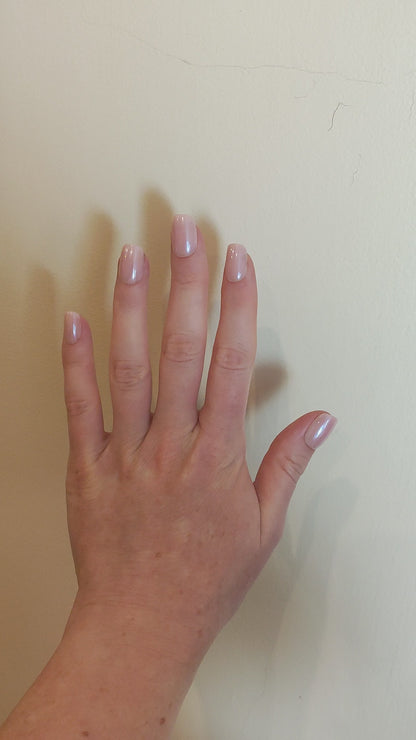 Left hand with square blush pink nails with a cream wall background.